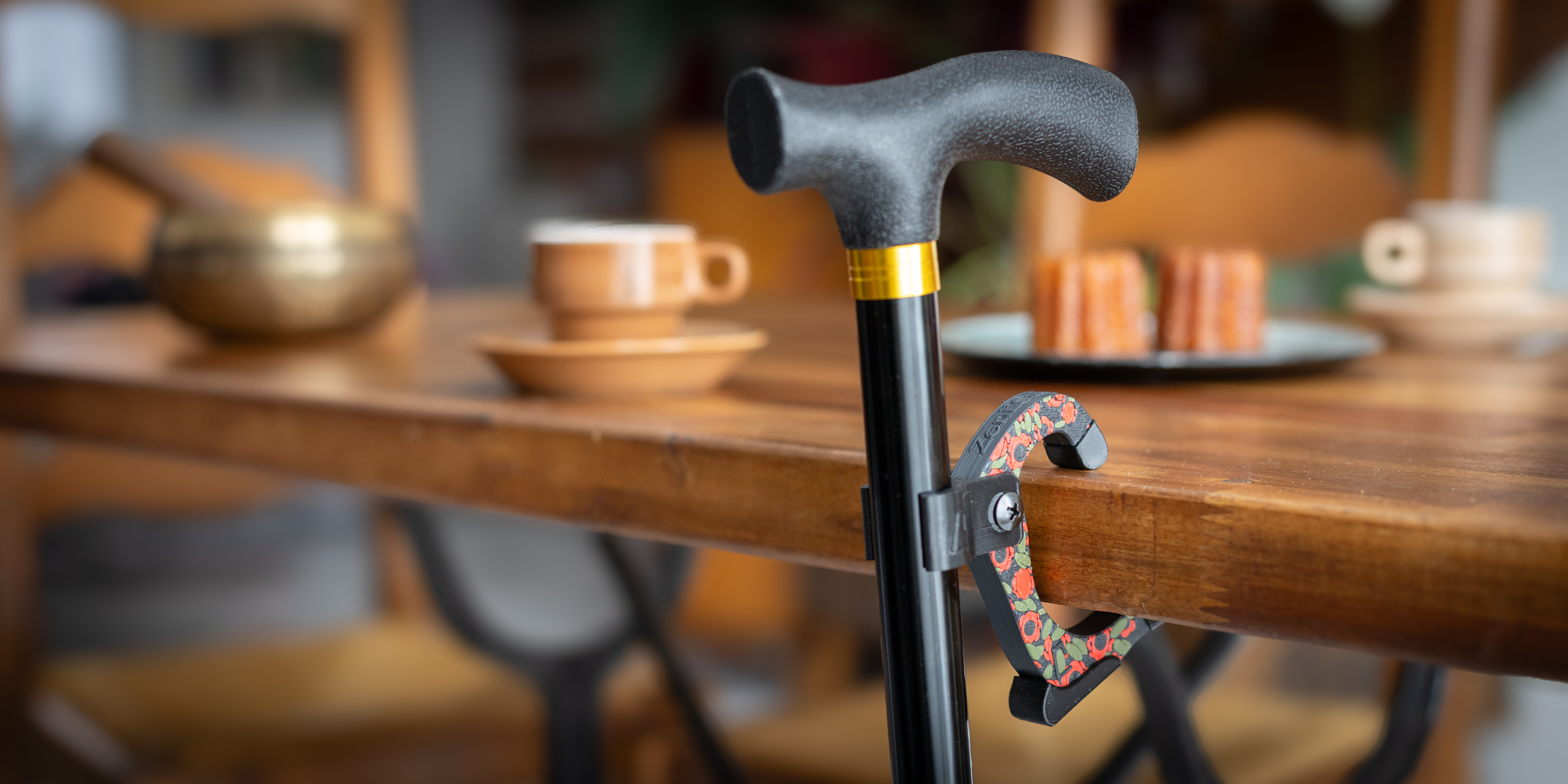 Accroche-canne Zeni’Clip fixé sur une canne, posée sur une table de café